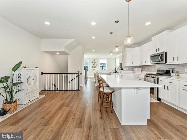 kitchen featuring appliances with stainless steel finishes, light wood-type flooring, a kitchen breakfast bar, pendant lighting, and white cabinets