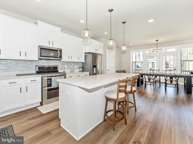 kitchen featuring stainless steel appliances, decorative light fixtures, white cabinets, a center island, and light hardwood / wood-style floors