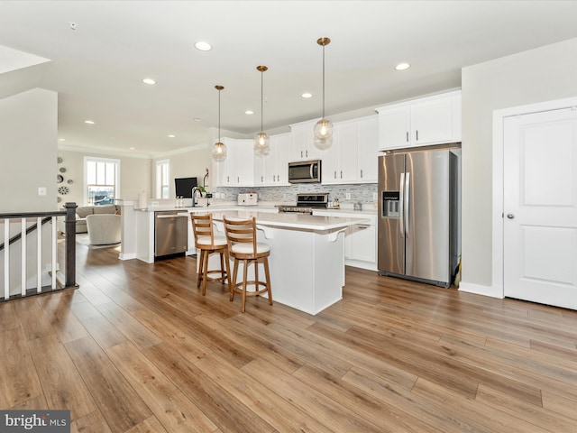 kitchen featuring white cabinetry, stainless steel appliances, kitchen peninsula, pendant lighting, and light wood-type flooring