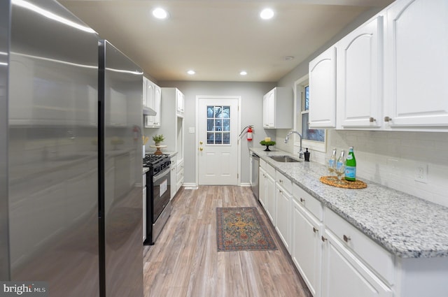 kitchen with white cabinets, sink, light stone countertops, appliances with stainless steel finishes, and light hardwood / wood-style floors