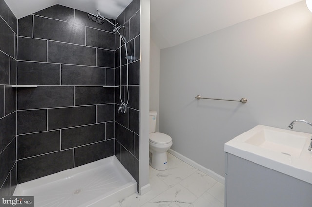 bathroom featuring a tile shower, vanity, lofted ceiling, and toilet