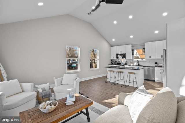 living room featuring light wood-type flooring, a wealth of natural light, ceiling fan, sink, and lofted ceiling