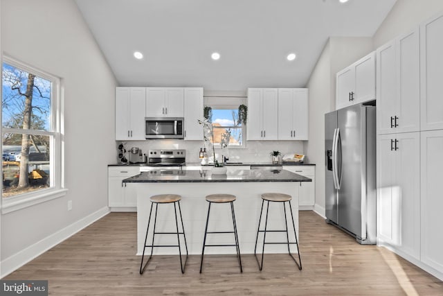 kitchen with stainless steel appliances, vaulted ceiling, white cabinetry, and a kitchen island