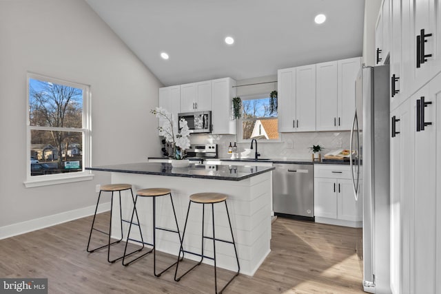 kitchen with white cabinetry, a center island, vaulted ceiling, a breakfast bar area, and appliances with stainless steel finishes