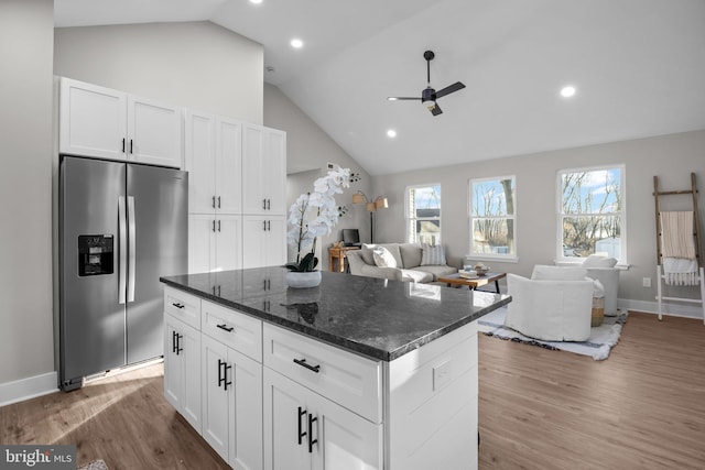 kitchen featuring dark stone counters, ceiling fan, stainless steel fridge with ice dispenser, a center island, and white cabinetry