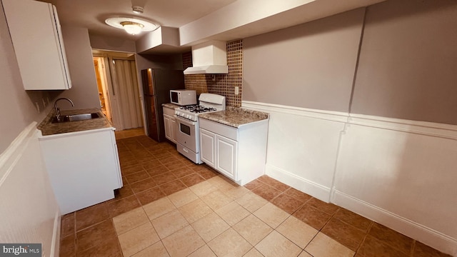 kitchen featuring wall chimney exhaust hood, white appliances, sink, white cabinets, and tile patterned flooring