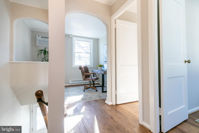 corridor featuring a wall unit AC, a baseboard heating unit, ornamental molding, and hardwood / wood-style flooring