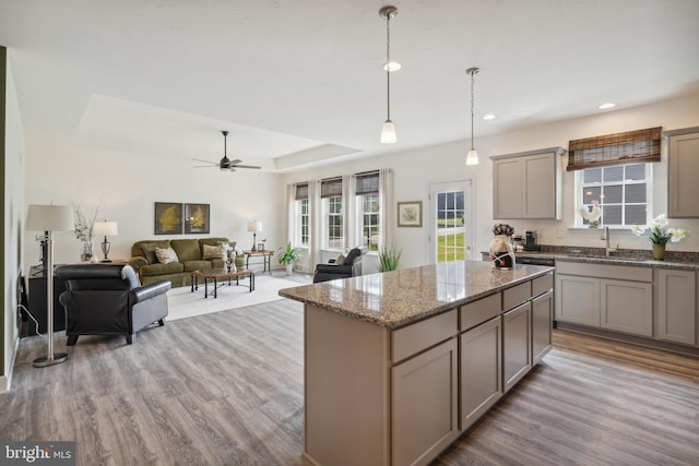 kitchen featuring ceiling fan, a tray ceiling, decorative light fixtures, a kitchen island, and light stone counters