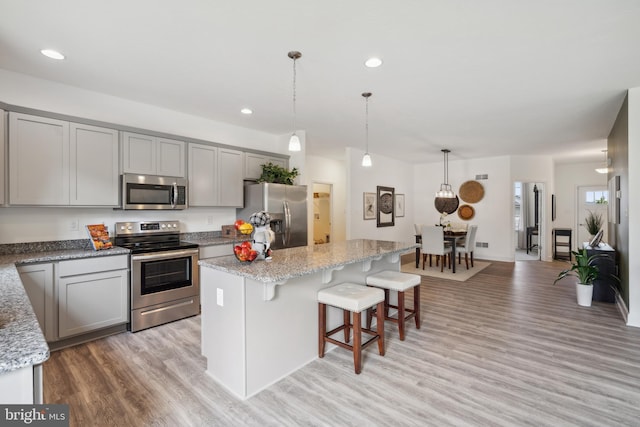 kitchen featuring light stone countertops, decorative light fixtures, a center island, and stainless steel appliances