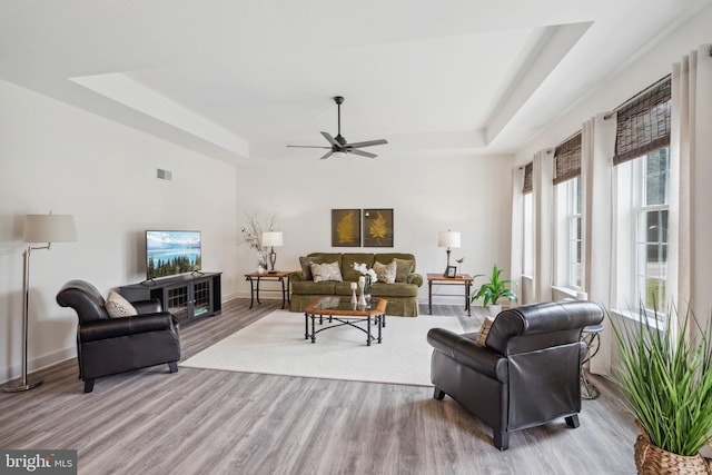 living room featuring a tray ceiling, ceiling fan, and light hardwood / wood-style flooring