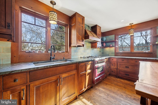 kitchen featuring sink, light hardwood / wood-style flooring, stainless steel range, decorative light fixtures, and custom range hood