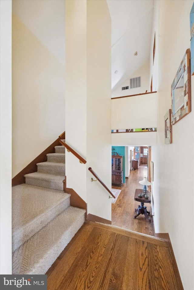 staircase with hardwood / wood-style flooring and high vaulted ceiling