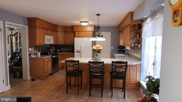 kitchen with white appliances, backsplash, sink, hanging light fixtures, and a breakfast bar area