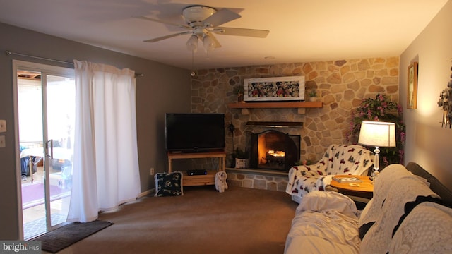 carpeted living room featuring a stone fireplace and ceiling fan