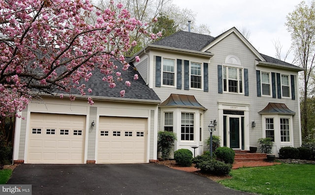 colonial inspired home featuring aphalt driveway, roof with shingles, and an attached garage