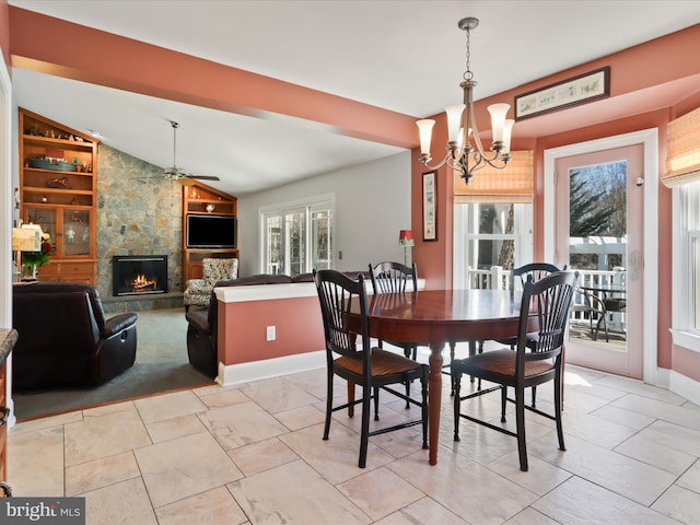 dining room with lofted ceiling, baseboards, ceiling fan with notable chandelier, and a stone fireplace