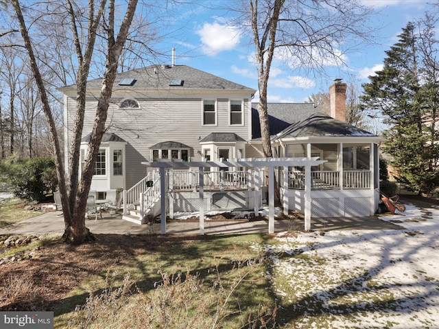 back of property with a patio, a shingled roof, a sunroom, a wooden deck, and a chimney