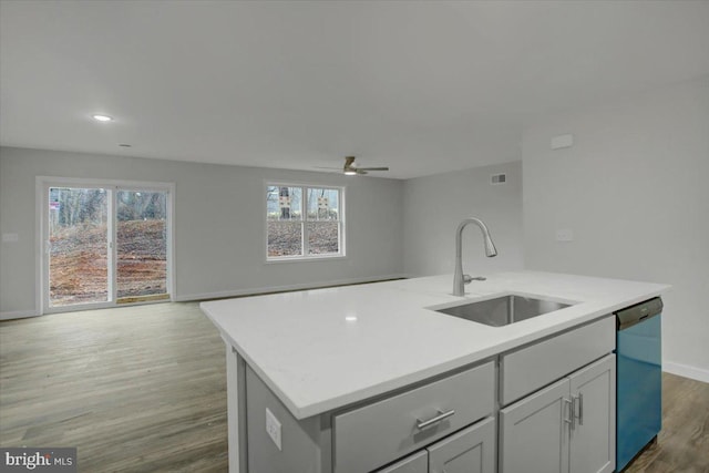 kitchen featuring ceiling fan, sink, stainless steel dishwasher, hardwood / wood-style floors, and a center island with sink