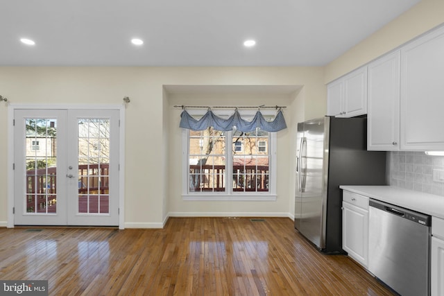 kitchen featuring appliances with stainless steel finishes, white cabinetry, hardwood / wood-style floors, decorative backsplash, and french doors