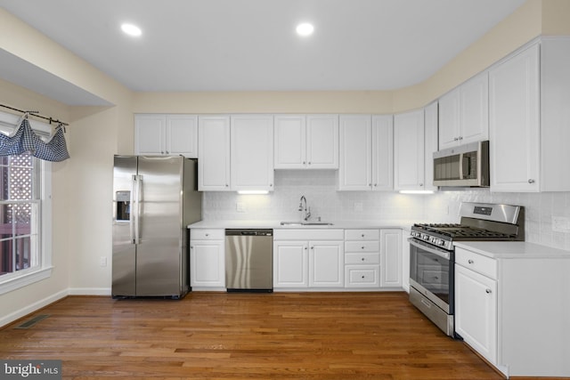 kitchen with stainless steel appliances, sink, hardwood / wood-style floors, and white cabinets