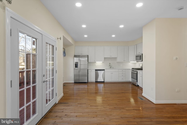 kitchen featuring appliances with stainless steel finishes, white cabinetry, backsplash, hardwood / wood-style floors, and french doors