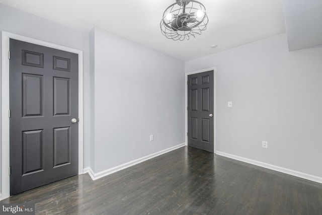 empty room with dark hardwood / wood-style flooring and an inviting chandelier