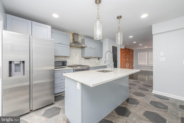 kitchen with light stone countertops, sink, wall chimney exhaust hood, stainless steel appliances, and an island with sink