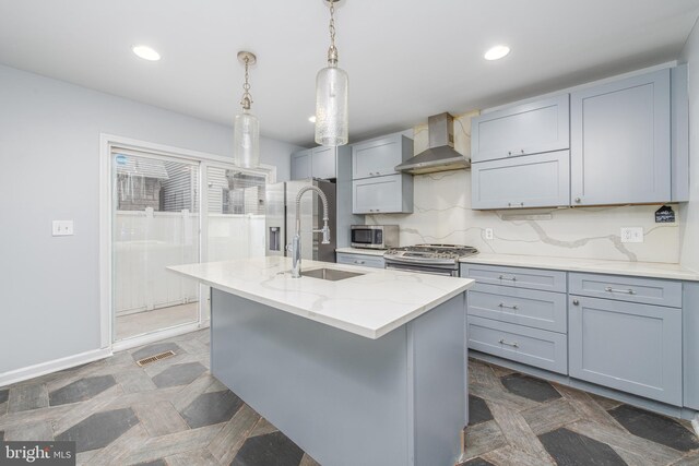 kitchen with sink, wall chimney exhaust hood, stainless steel appliances, light stone counters, and decorative light fixtures