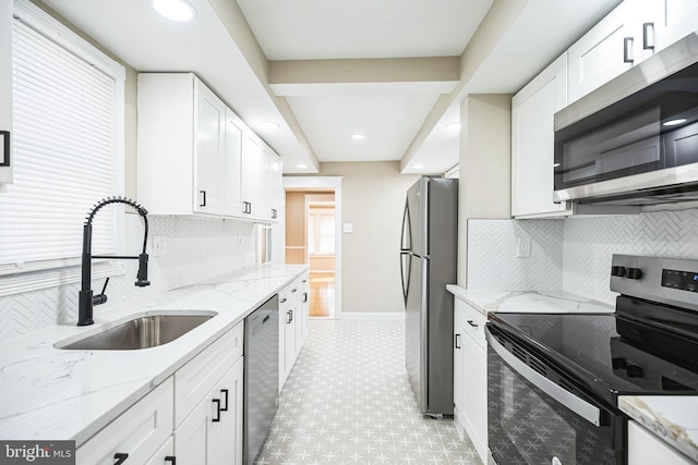 kitchen with light stone countertops, appliances with stainless steel finishes, decorative backsplash, sink, and white cabinetry