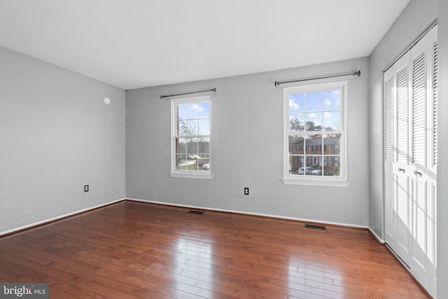 unfurnished bedroom featuring multiple windows, hardwood / wood-style floors, and a closet