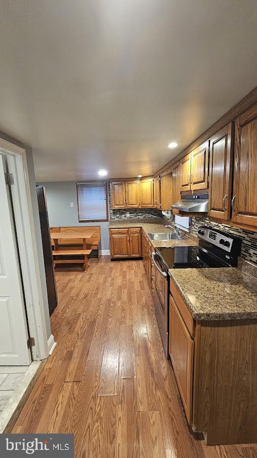 kitchen featuring electric stove, sink, dark stone countertops, and light hardwood / wood-style flooring