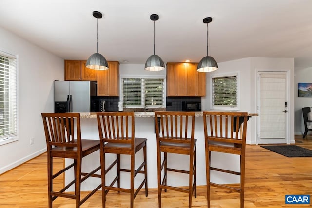 kitchen featuring stainless steel fridge with ice dispenser, light hardwood / wood-style floors, decorative light fixtures, a breakfast bar area, and decorative backsplash