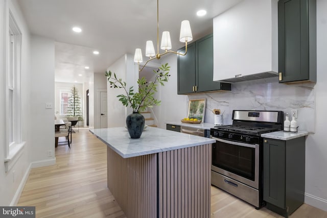 kitchen with backsplash, gas stove, wall chimney range hood, decorative light fixtures, and a center island