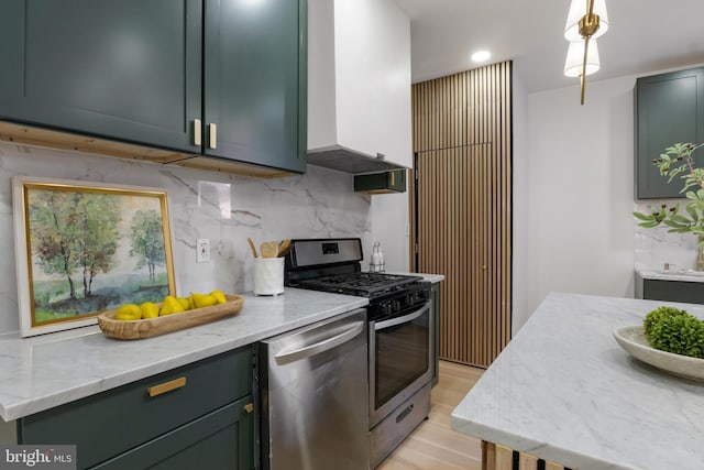 kitchen with decorative backsplash, appliances with stainless steel finishes, light stone countertops, wall chimney exhaust hood, and decorative light fixtures