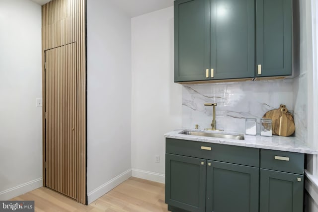 bar with green cabinets, sink, decorative backsplash, light wood-type flooring, and light stone counters