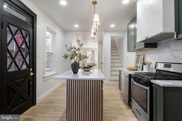 kitchen featuring light wood-type flooring, stainless steel appliances, hanging light fixtures, and wall chimney exhaust hood