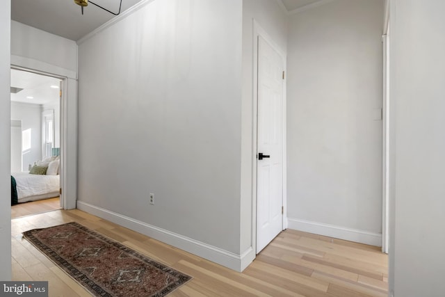 corridor featuring a notable chandelier, light wood-type flooring, and crown molding