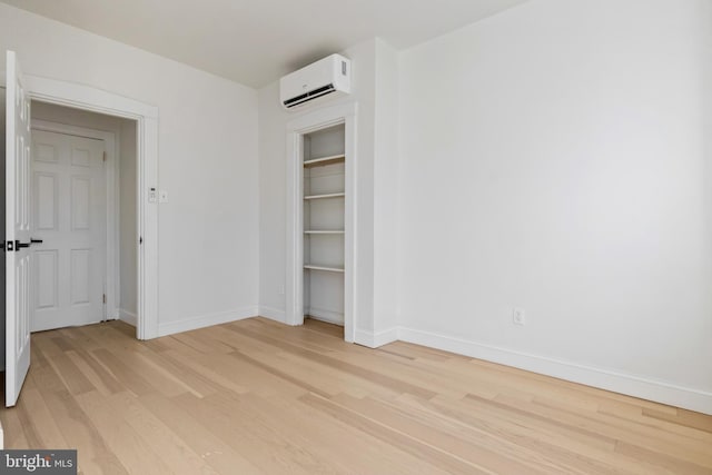 unfurnished bedroom with light hardwood / wood-style flooring, an AC wall unit, and a closet