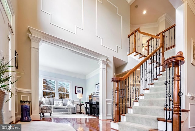 staircase with wood-type flooring, ornate columns, and ornamental molding