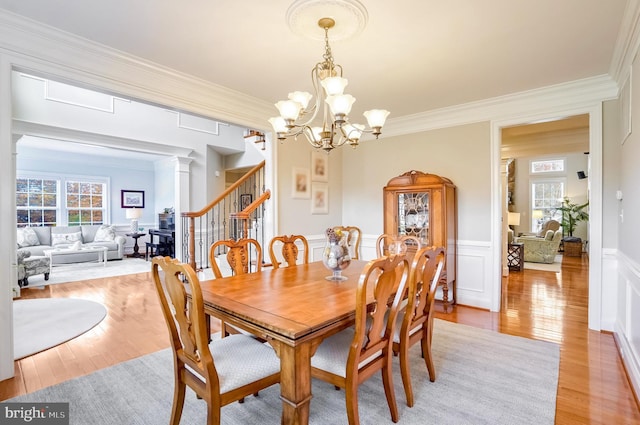 dining area with a notable chandelier, light wood-type flooring, ornamental molding, and ornate columns