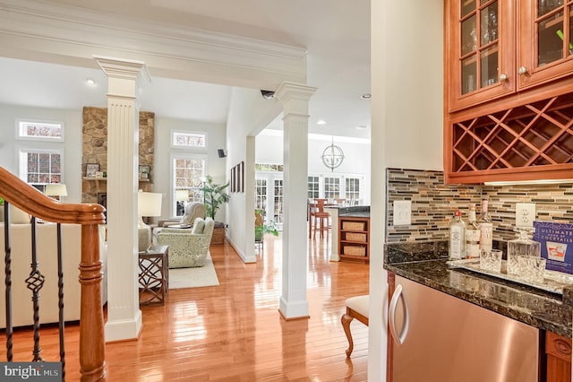 bar with ornate columns, light hardwood / wood-style flooring, dark stone counters, and tasteful backsplash