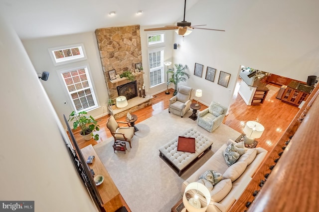 living room with a stone fireplace, ceiling fan, a towering ceiling, and wood-type flooring