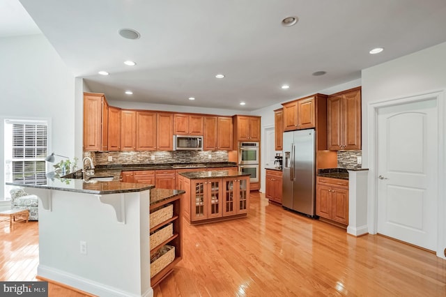 kitchen with stainless steel appliances, kitchen peninsula, dark stone counters, light hardwood / wood-style floors, and a kitchen bar