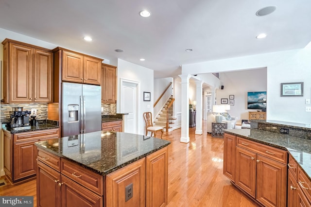 kitchen with backsplash, dark stone counters, light wood-type flooring, ornate columns, and stainless steel fridge with ice dispenser