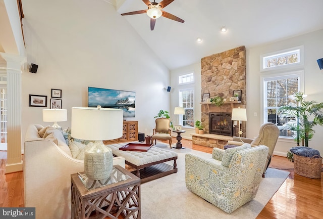 living room with ceiling fan, a stone fireplace, high vaulted ceiling, decorative columns, and light hardwood / wood-style floors