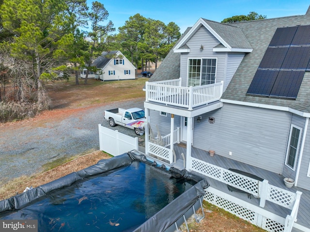 rear view of house featuring solar panels, a balcony, and a covered pool