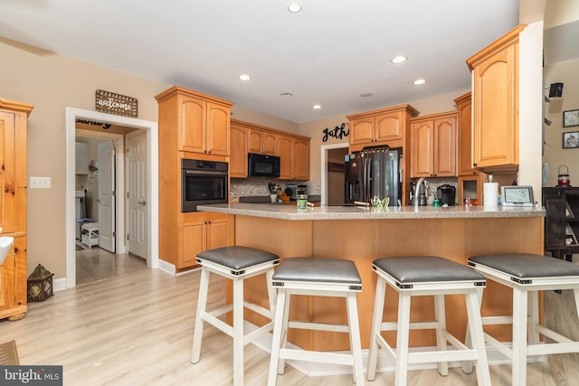 kitchen with kitchen peninsula, light hardwood / wood-style floors, a breakfast bar area, decorative backsplash, and black appliances