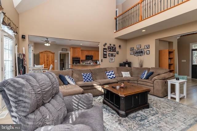 living room with ceiling fan, light hardwood / wood-style floors, and a high ceiling