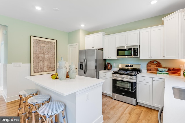 kitchen with appliances with stainless steel finishes, a kitchen breakfast bar, light hardwood / wood-style flooring, white cabinets, and a kitchen island