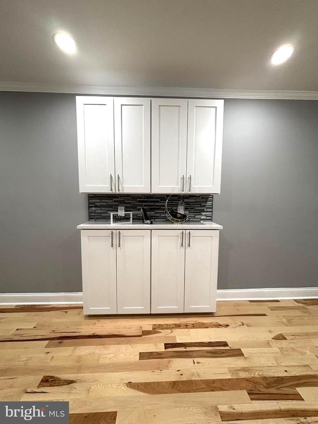 bar featuring decorative backsplash, crown molding, light hardwood / wood-style flooring, and white cabinets